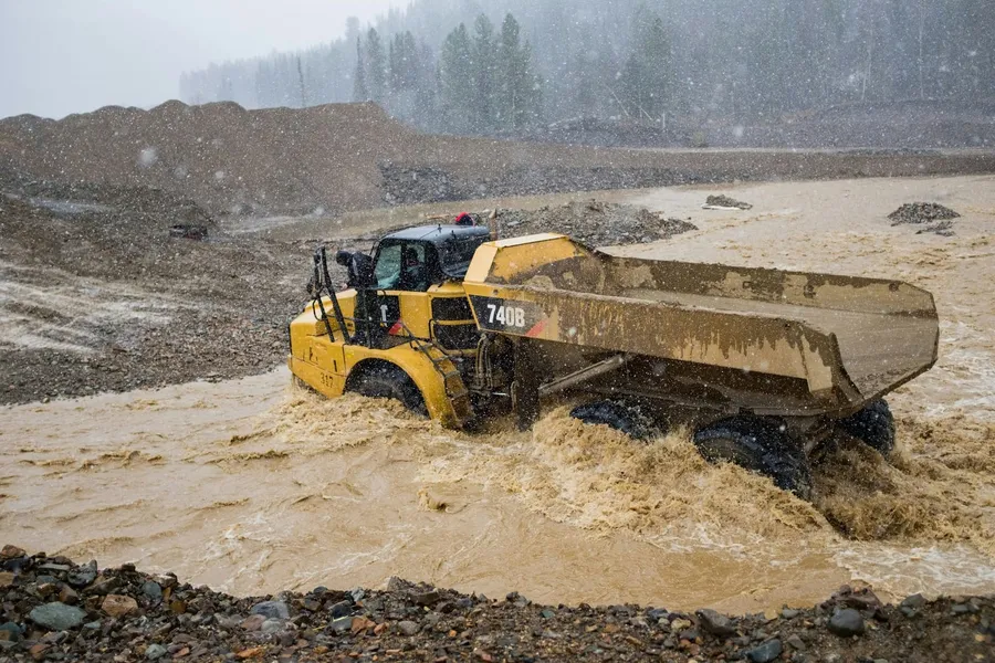 Articulated dump truck driving through deep muddy water in heavy rain
